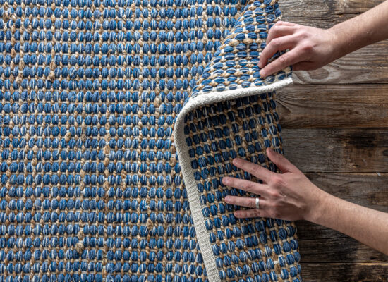 Man rolling carpet on floor in room, top view, fragment colored carpet, bright wicker blue rug.